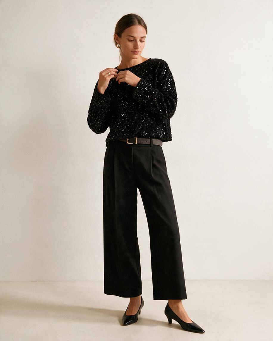 Modelo vistiendo blusa negra de lentejuelas de Yanet Collective con pantalones anchos y tacones