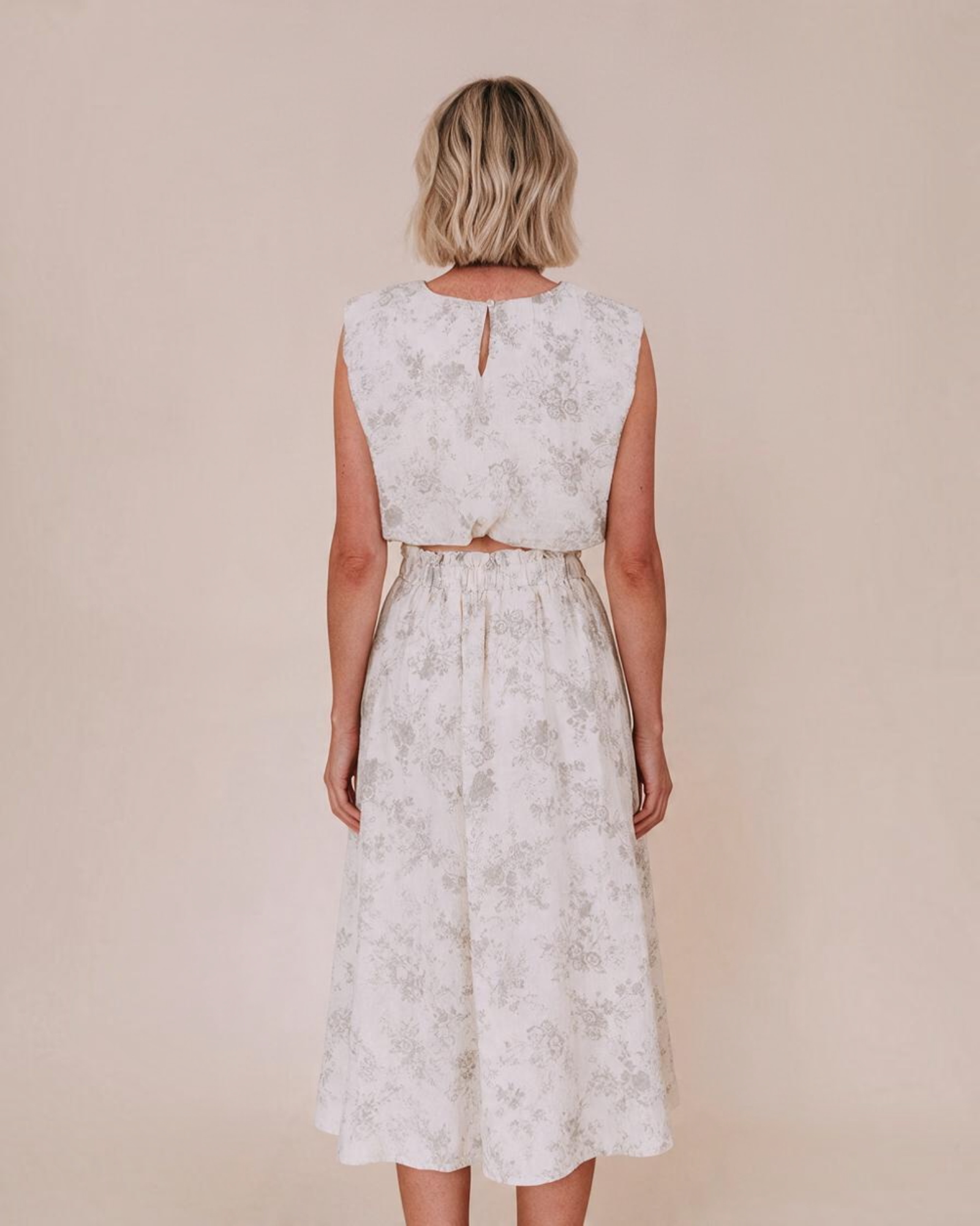 Vista trasera de mujer con top corto sin mangas Yanet Collective blanco con estampado floral y falda a juego